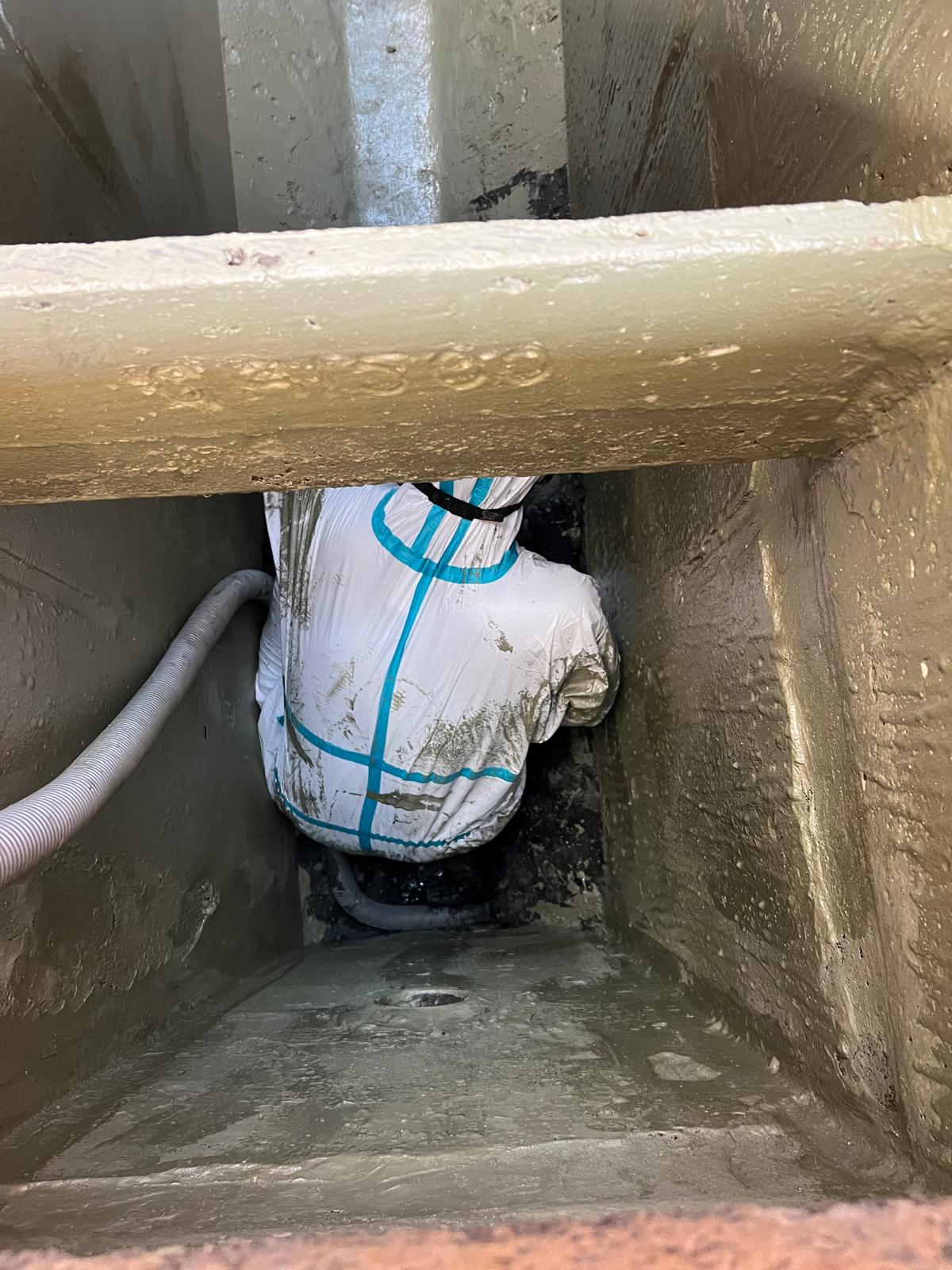 Technician applying protective coating inside a grease trap via confined space entry